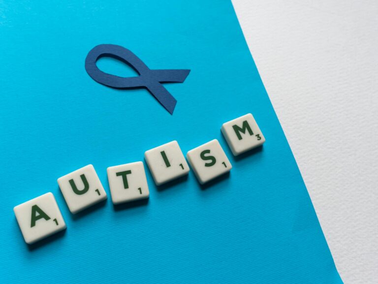 Close-up of autism awareness concept with blue ribbon and Scrabble tiles spelling 'AUTISM'.