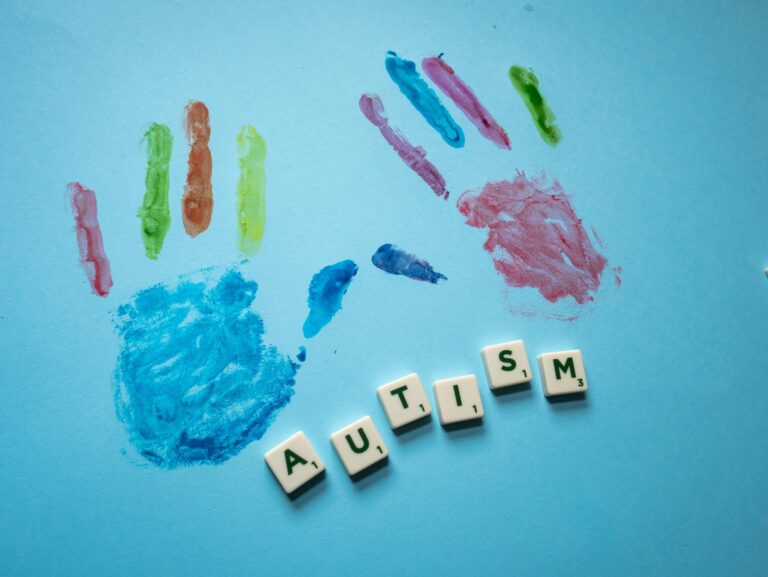 Colorful child handprints and autism text on a blue background, promoting awareness.